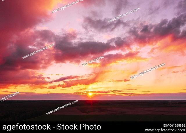 Sunset sunrise colorful sky over field or meadow. Bright dramatic sky and dark ground. Countryside landscape under scenic amazing natural bright dramatic...