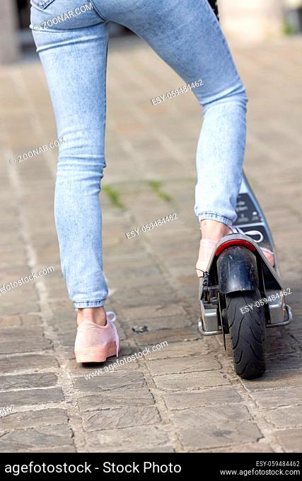 Close-up of female feet of a girl wearing pink sneakers and a jeans on electric kick scooter on the background of the city streets. High quality photo