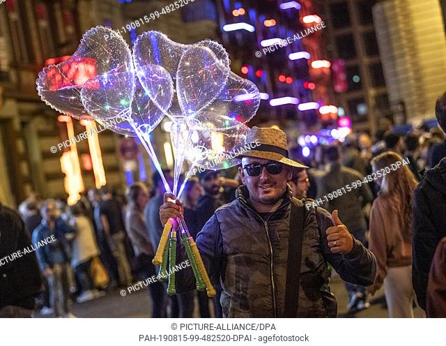 15 August 2019, Hessen, Frankfurt/Main: A man sells heart-shaped balloons on station quarter night. Every year the Frankfurters celebrate the railway station...