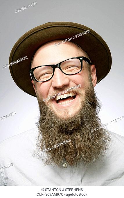 Studio portrait of laughing mid adult man in trilby with overgrown beard