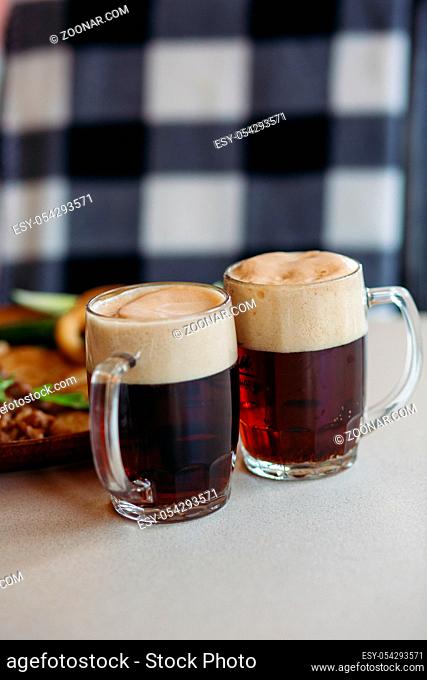 Two big glass cups full of foamy cold beer standing on light smooth table surface in restaurant or pub. Big plate with delicious appetizers like potato puncakes...