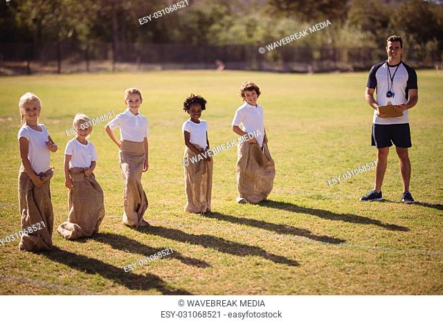 Portrait of coach and schoolgirls standing in park during sack race