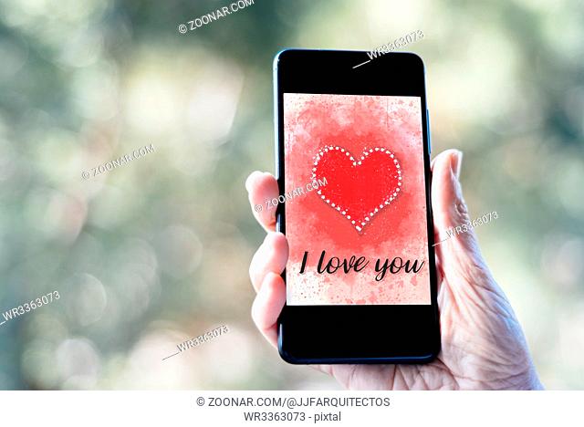 Valentines day sale background with woman hand holding smartphone with heart illustration with the words I Love You on screen mockup against nature background
