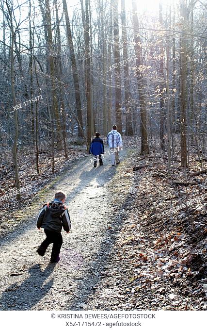 A young boy runs to catch up to his Father and older brother on a wooded trail
