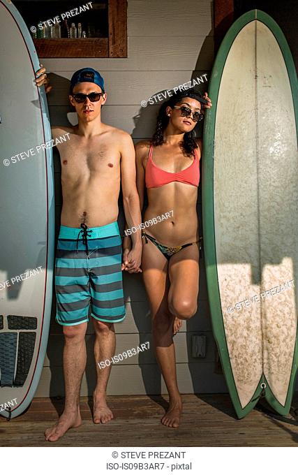Portrait of cool young surfing couple standing on porch, Rockaway Beach, New York State, USA