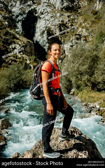 Smiling woman with backpack standing against river at Cares Trail in Picos De Europe National Park, Asturias, Spain
