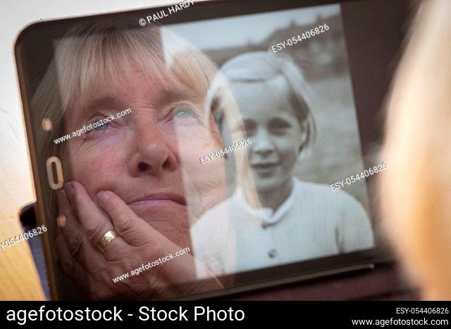 Senior caucasian woman looking at old photos of her younger self on a tablet computer themes of contrasts the ageing process nostalgia and childhood