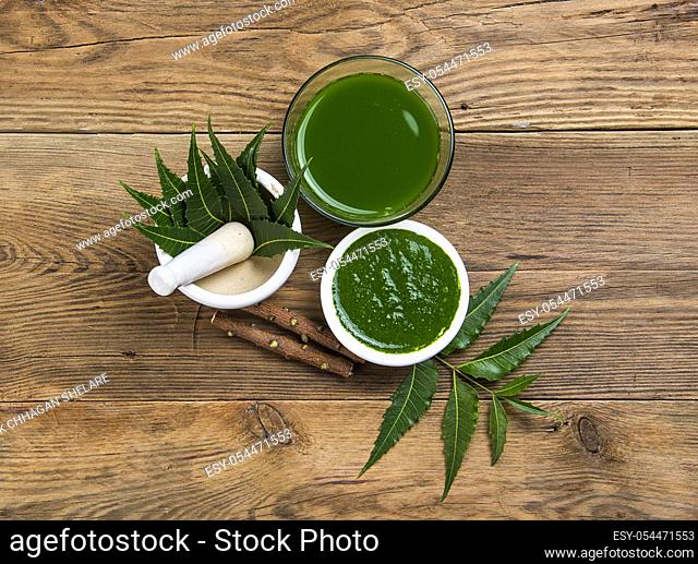 Medicinal Neem leaves in mortar and pestle with neem paste, juice and twigs on wooden background