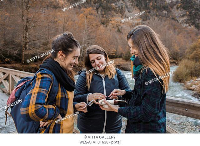 Spain, three young women looking at instant photos on a bridge in Ordesa National Park