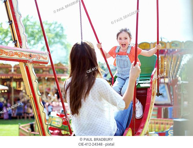 Mother and daughter playing on swing in amusement park