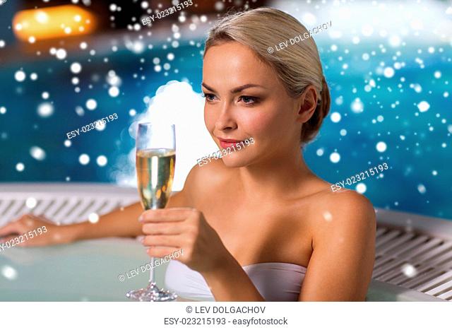 people, beauty, spa, healthy lifestyle and relaxation concept - beautiful young woman wearing bikini swimsuit sitting with glass of champagne in jacuzzi at...