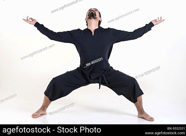 A man dressed in black doing yoga over white background. Utkata konasana yoga pose. Studio shot