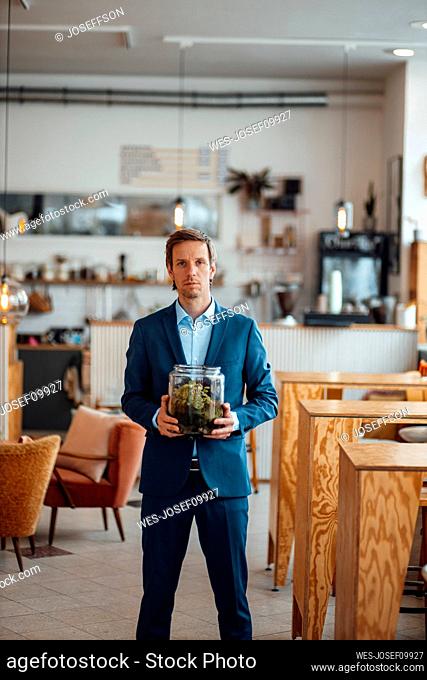 Mature businessman with plant in glass container standing at cafe