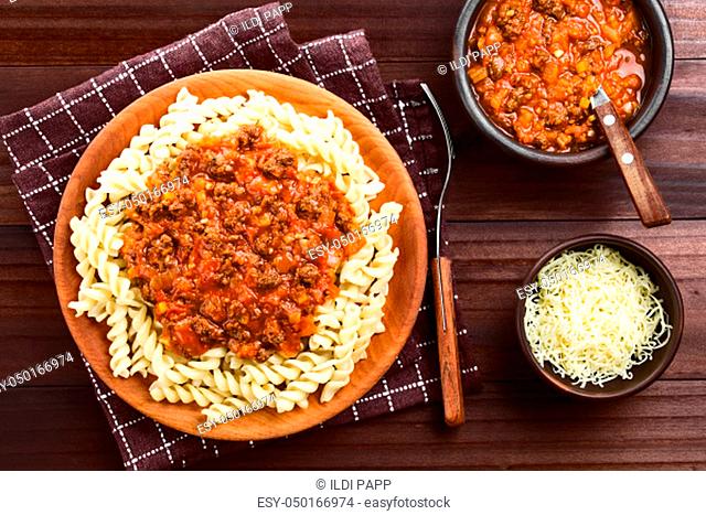 Homemade vegan bolognese sauce made with soy meat, fresh tomatoes, onion and garlic served on fusilli pasta on wooden plate, photographed overhead