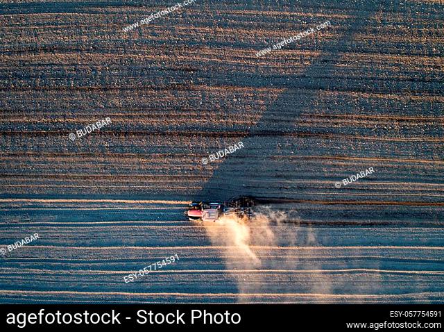 Aerial view of tractor harrowing arable land shot from drone directly above
