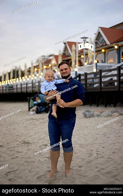 Smiling father with son standing on sand at beach