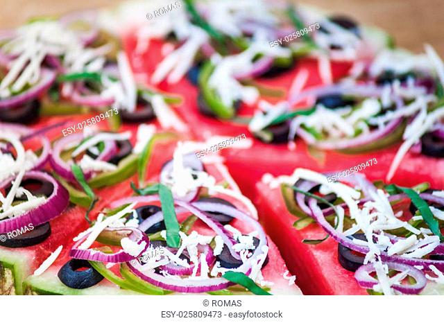 Sliced juicy watermelon pizza isolated on white, closeup view from above. Ingredients are watermelon, olives, bell pepper, cheese, basil
