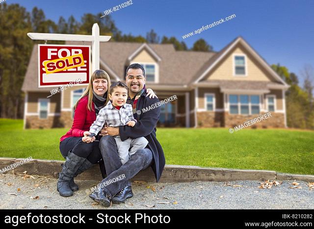 Happy mixed-race family in front of their new home and a sold for sale real estate sign