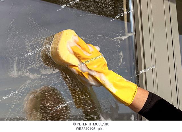 Hand wearing a yellow rubber glove and sponge cleaning a window