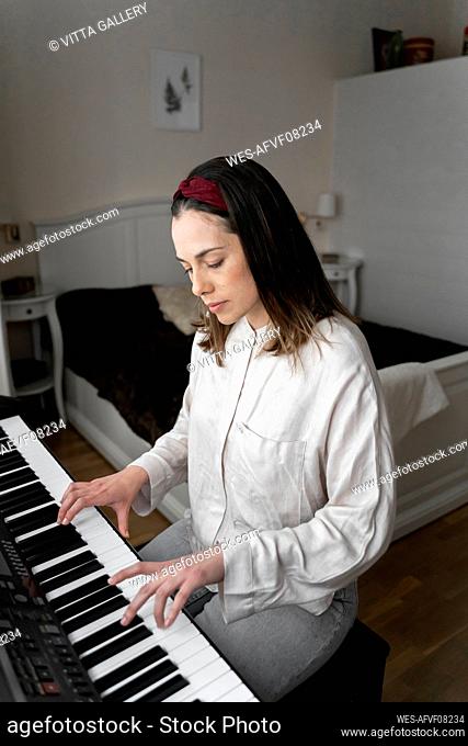 Woman playing piano while sitting in bedroom