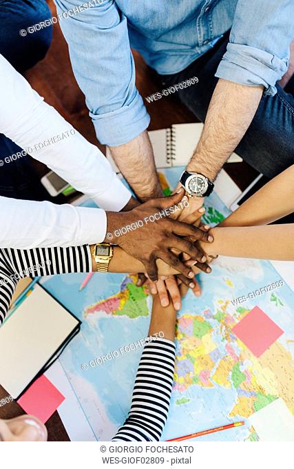 Group of friends stacking hands above world map