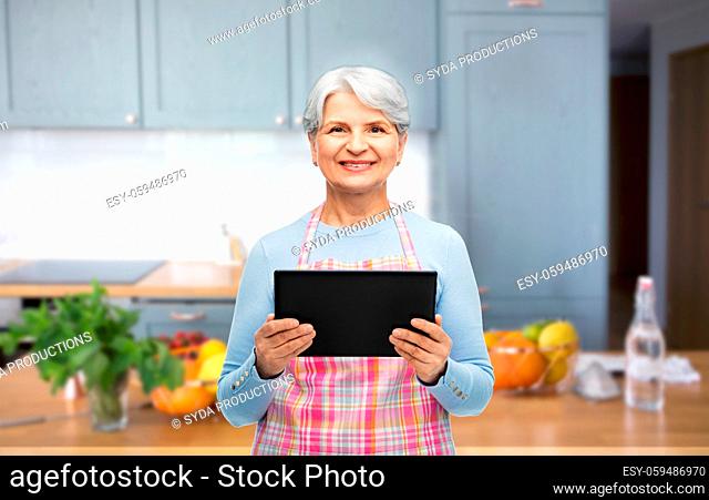 smiling senior woman with tablet pc at kitchen