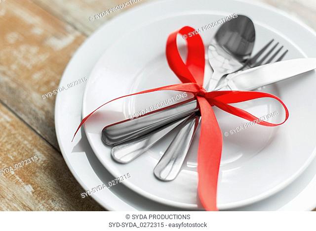 close up of cutlery tied with red ribbon on plates