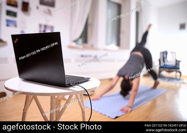 02 November 2020, Baden-Wuerttemberg, Stuttgart: A woman is warming up in front of a laptop with a yoga exercise for her yoga class