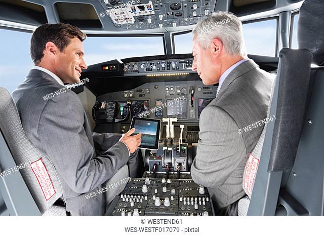 Germany, Bavaria, Munich, Businessmen showing digital table in airplane cockpit