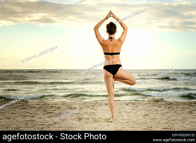 beautiful woman in a black swimsuit practicing yoga on the beach at sunset