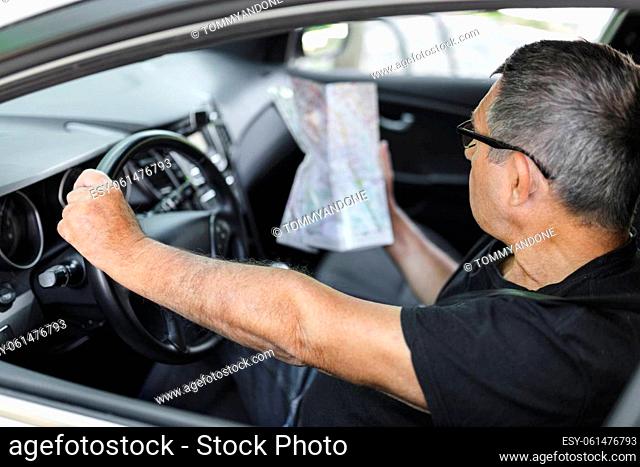 Senior behind the steering wheel of a car, looking at map for directions