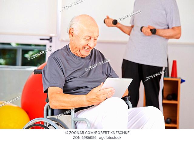 Behinderter Mann sitzt im Rollstuhl mit Tablet PC in einem Pflegeheim