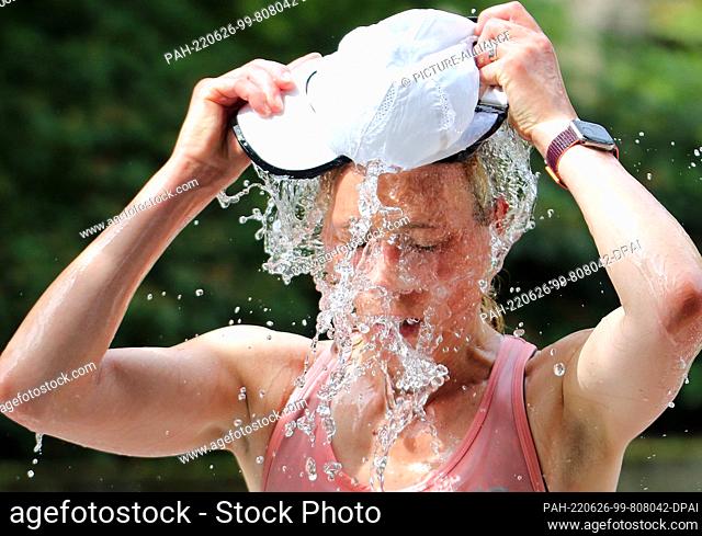26 June 2022, Hamburg, Au··enalster: Half marathon, Hamburg. A participant fills her cap with water at a refreshment station and tips it over her head