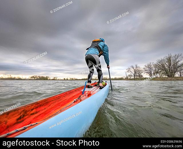 Gone paddling - low angle view from action camera of a male paddler on a long racing stand up paddleboard. Recreation, training and fitness i on a lake on...