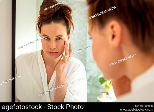 Woman touching her face while looking in the mirror