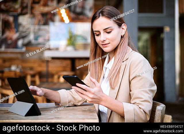 Businesswoman with digital tablet using smart phone at cafe terrace