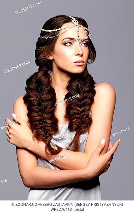 Beauty portrait of young woman with diadem. Brunette girl with long hair plaits and day female makeup on gray background
