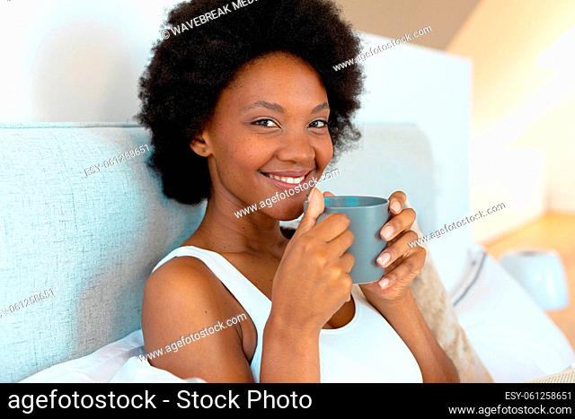 Portrait of smiling african american young afro woman having coffee in bedroom, copy space