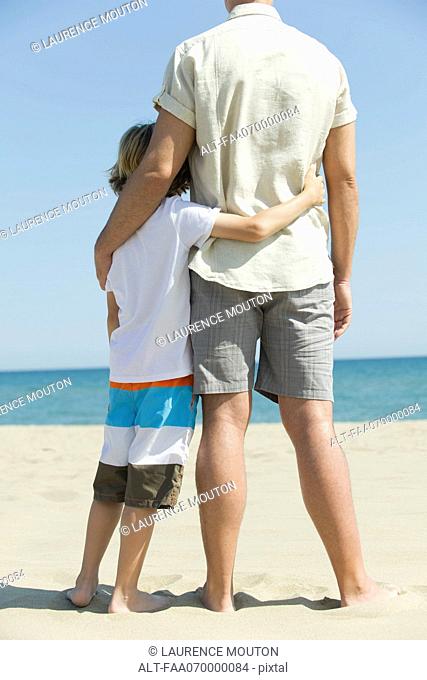 Father and young son standing together at the beach, rear view