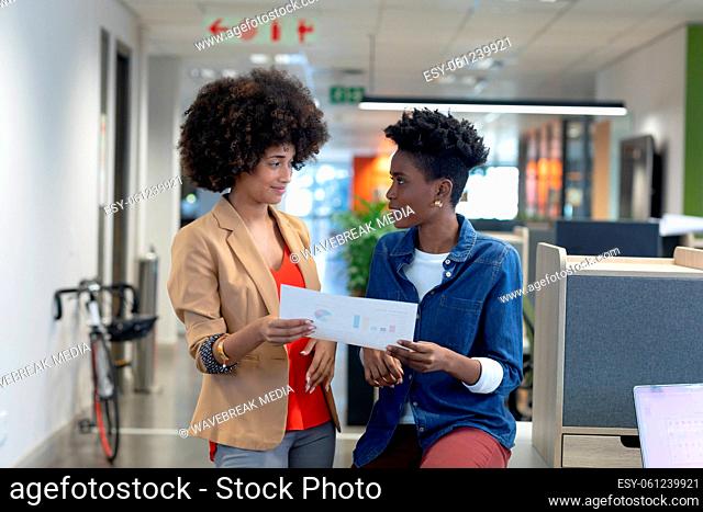 Multiracial businesswomen looking at each other while discussing over document at workplace