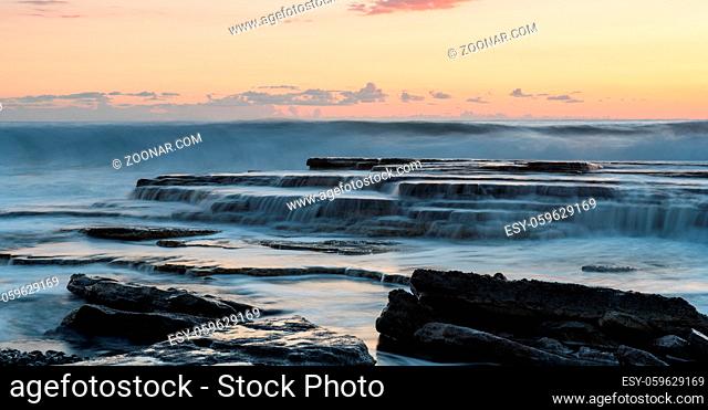 Rocky seashore seascape with wavy ocean and waves crashing on the rocks during a dramatic and beautiful sunset at Akrotiri coast area in Limassol, Cyprus