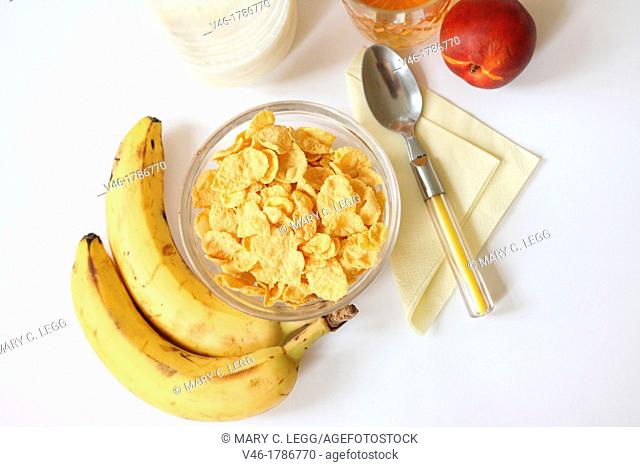 Breakfast cornflakes with milk and fruit  Cornflakes with bananas for healthy breakfast  Juice in lead glass  Nectarine  Yellow napkin with yellow flatware...
