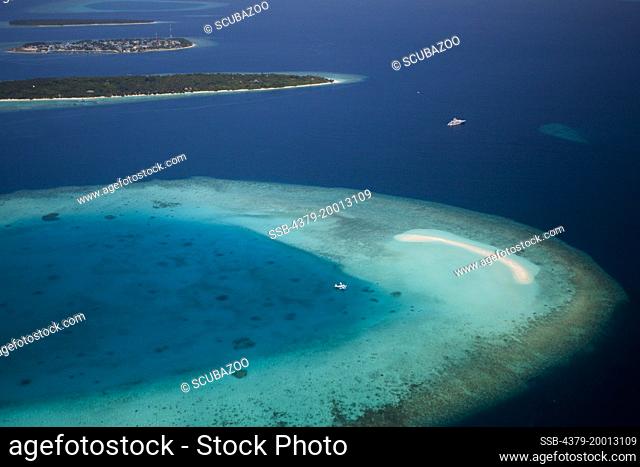 Aerial view of a seaplane moored in a lagoon next to a sandbank, with Soneva Fushi Resort, and Eydhafushi island in the background