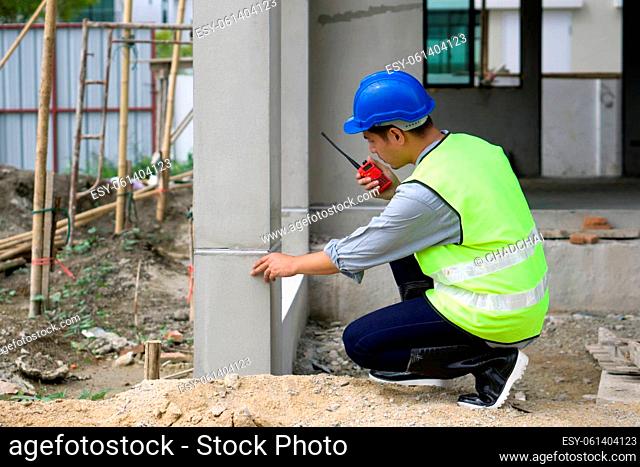 ??Young asian man in hardhat and safety vest checking house structure while holding Walkie-Talkie. Work environment of engineers at the construction site of...