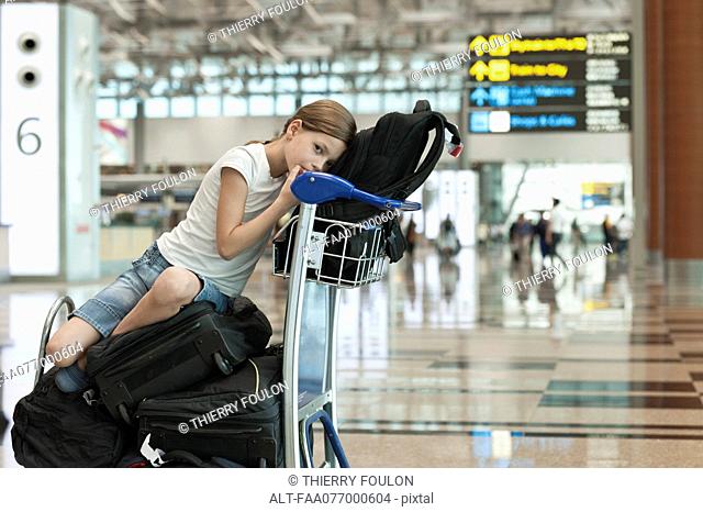 Girl sitting on top of luggage in airport