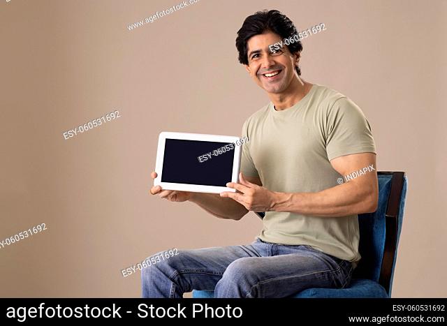 Indian man displaying his tablet while sitting on chair