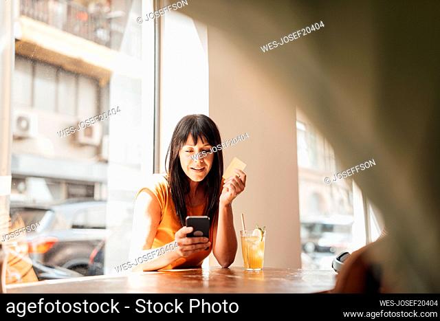 Smiling mature woman using smart phone at table in cafe