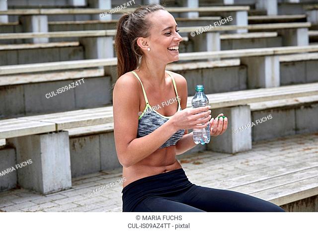 Young woman training, taking a water break on stadium stairway