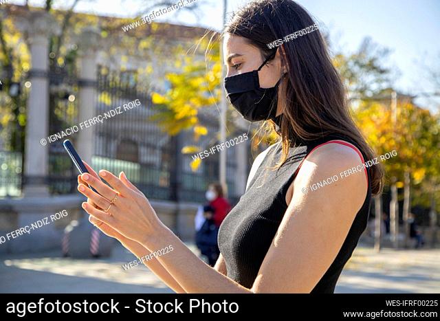 Young woman wearing face mask using smart phone while standing on street