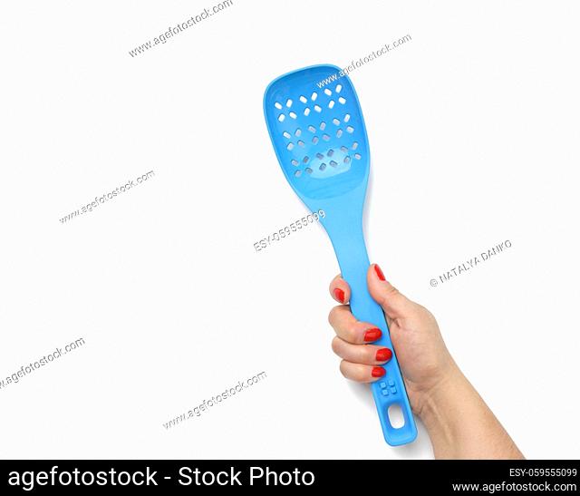 female hand holding a blue plastic spatula with holes on a white background